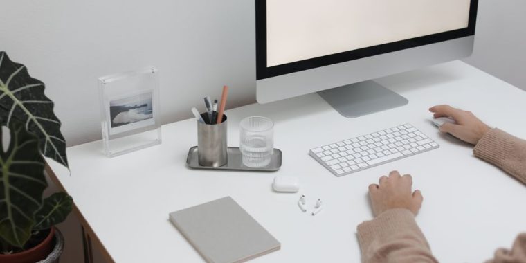 High angle of crop faceless person sitting at table with wireless gadgets and computer
